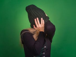 The woman covers her face with a knitted hat and turns away